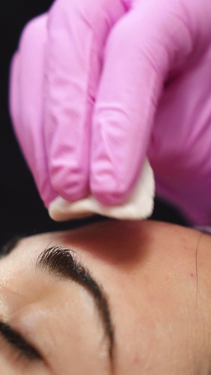 Female cosmetologist using ultrasonic scrubber on client's face. Professional ultrasonic equipment. Vertical video