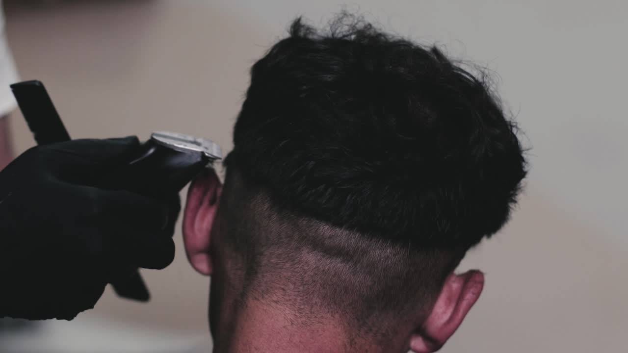 peluquero que usa maquinillas eléctricas para cortar el cabello de un cliente masculino en su barbería