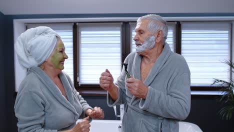 elderly grandmother with facial green mask and grandfather with shaving foam dancing in bathroom
