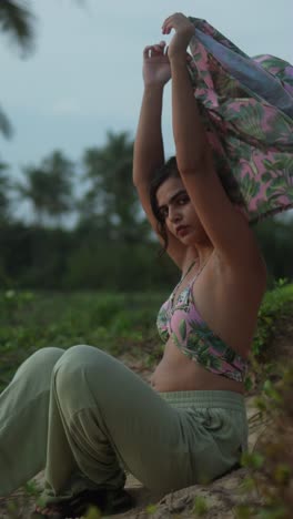 a woman practices aerial yoga outdoors with a focused expression, surrounded by palm trees, vertical shot