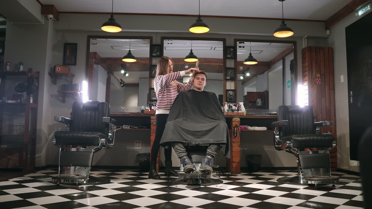 fotografía interior del proceso de trabajo en una barbería moderna. retrato de un joven atractivo con un corte de pelo de moda. un peluquero masculino sirviendo al cliente, haciendo un corte de pelo con tijeras de metal y peine.