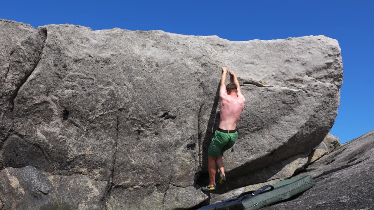 joven boulder en roca sin camisa con clima soleado en la playa rocosa