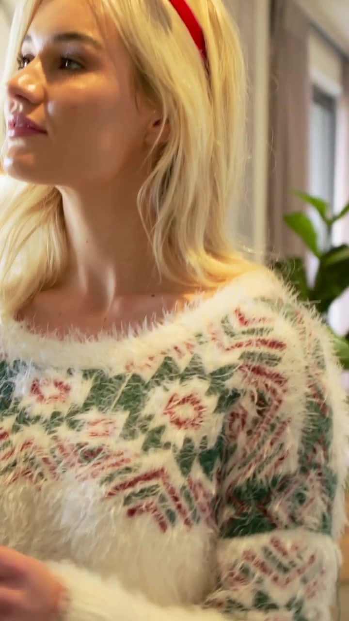 Vertikales Video: Blickt nach links, Frau in festlichem Pullover hält beleuchteten Mini-Kranz, dekoriert Spiegel.