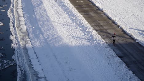 Joggende-Frau-Läuft-Im-Winter-Neben-Dem-Zugefrorenen-Fluss-Mit-Eisschollen