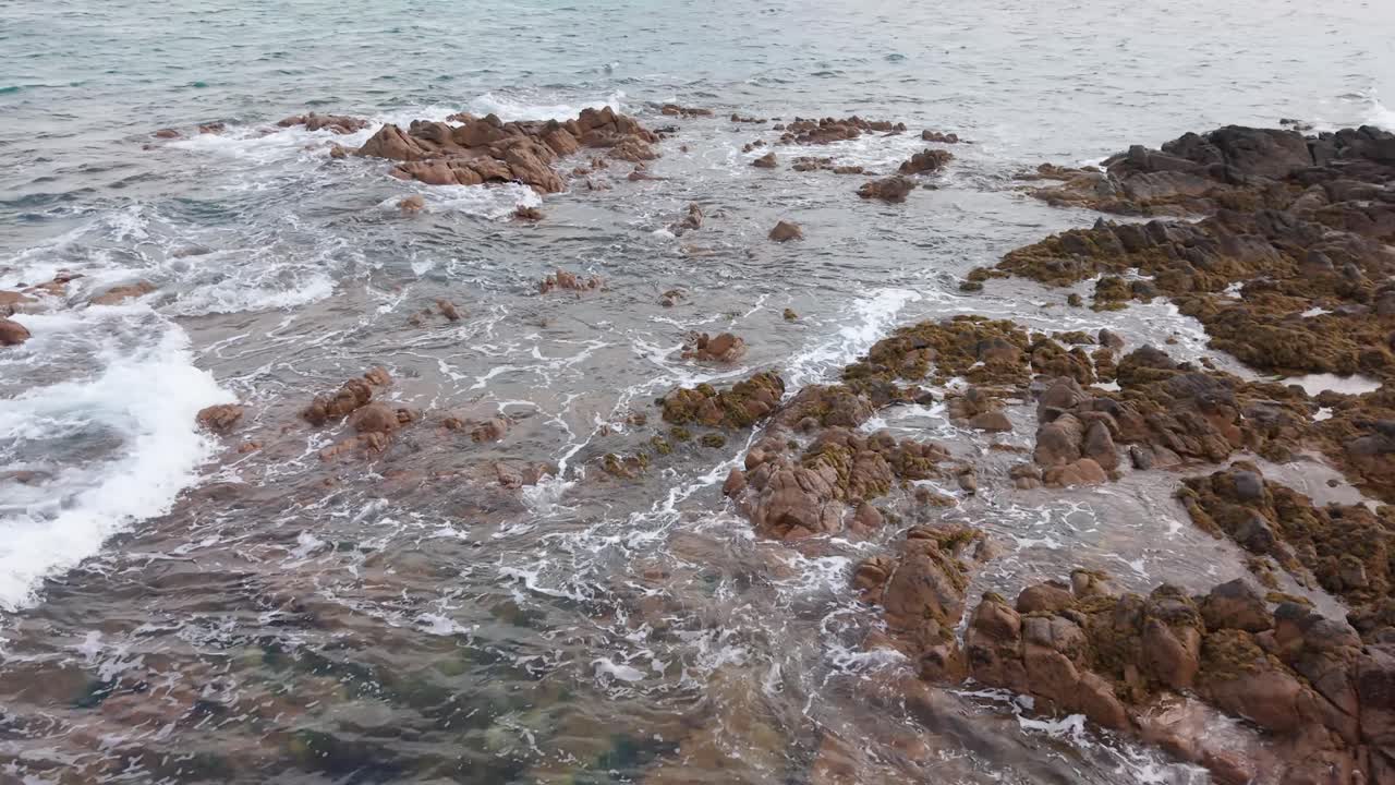 Waves lapping over granite outcrop on calm bright day panning round to rockpools and inlets