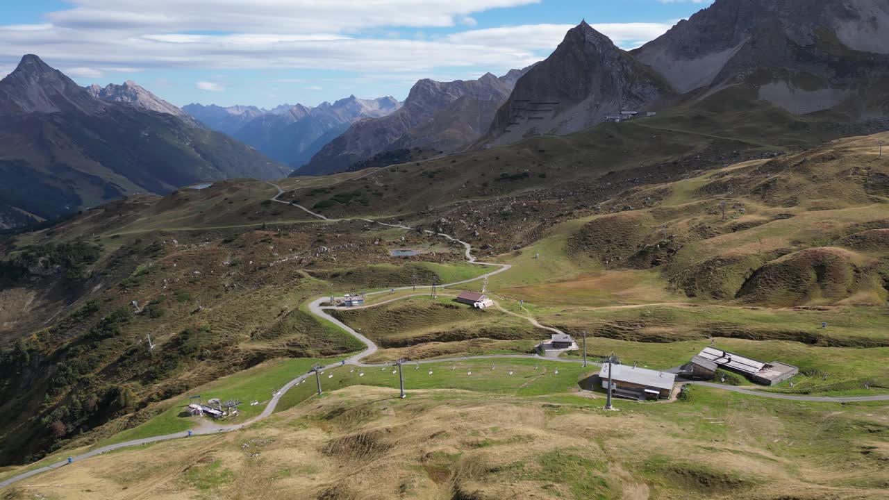 una impresionante vista aérea de warth, vorarlberg en austria, que muestra los majestuosos alpes montañosos, viviendas residenciales dispersas y un cielo azul claro con nubes finas en el horizonte