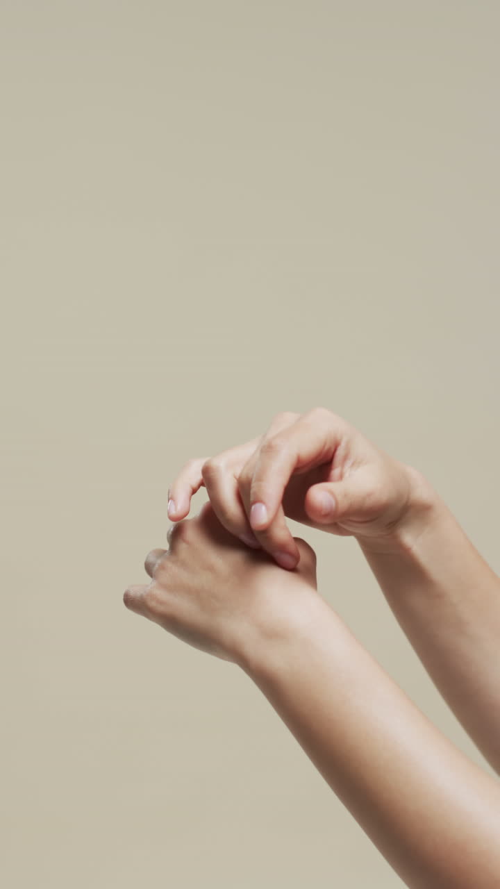 Vertical video of hands of biracial woman on beige background with copy space, slow motion