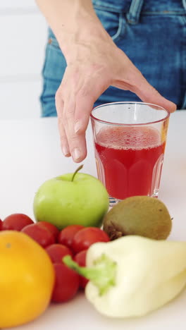 Woman hand takes a glass of fresh juice from the kitchen table with fruits. Vertical video