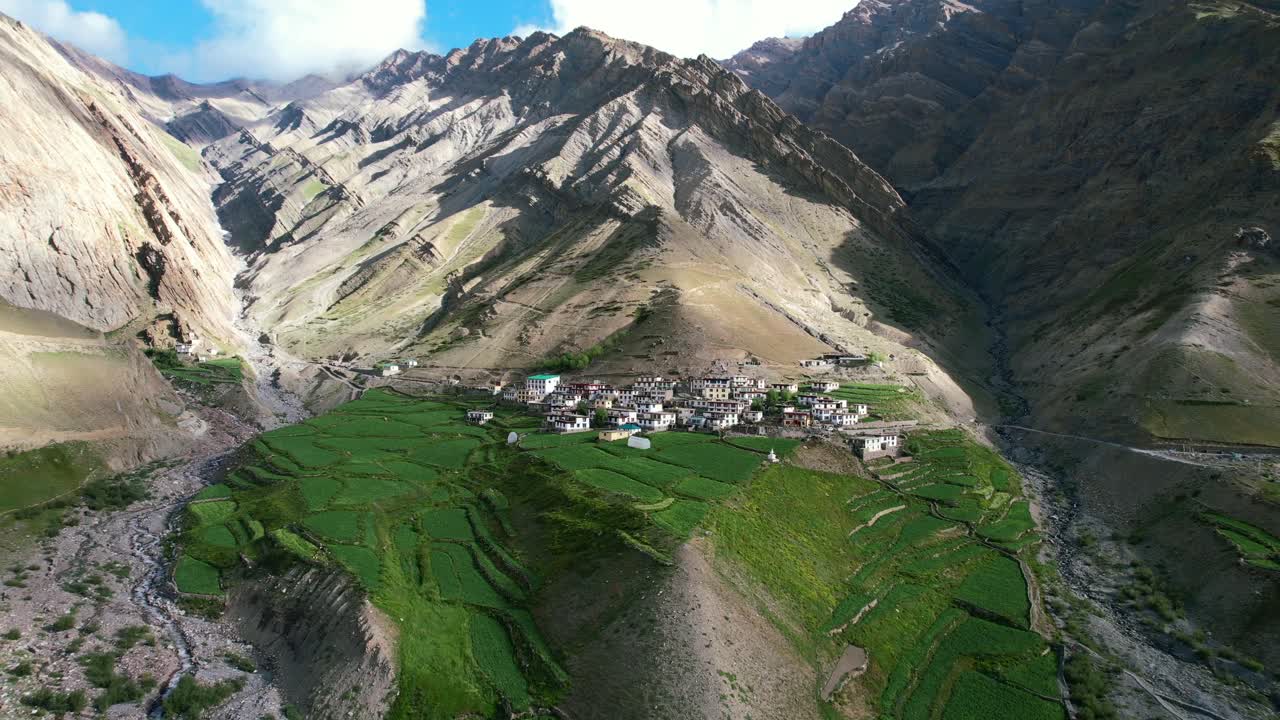 aerial dolly zoom out of Mud Village in the remote mountains of Pin Valley on sunny day with lush green ricefields and farmland
