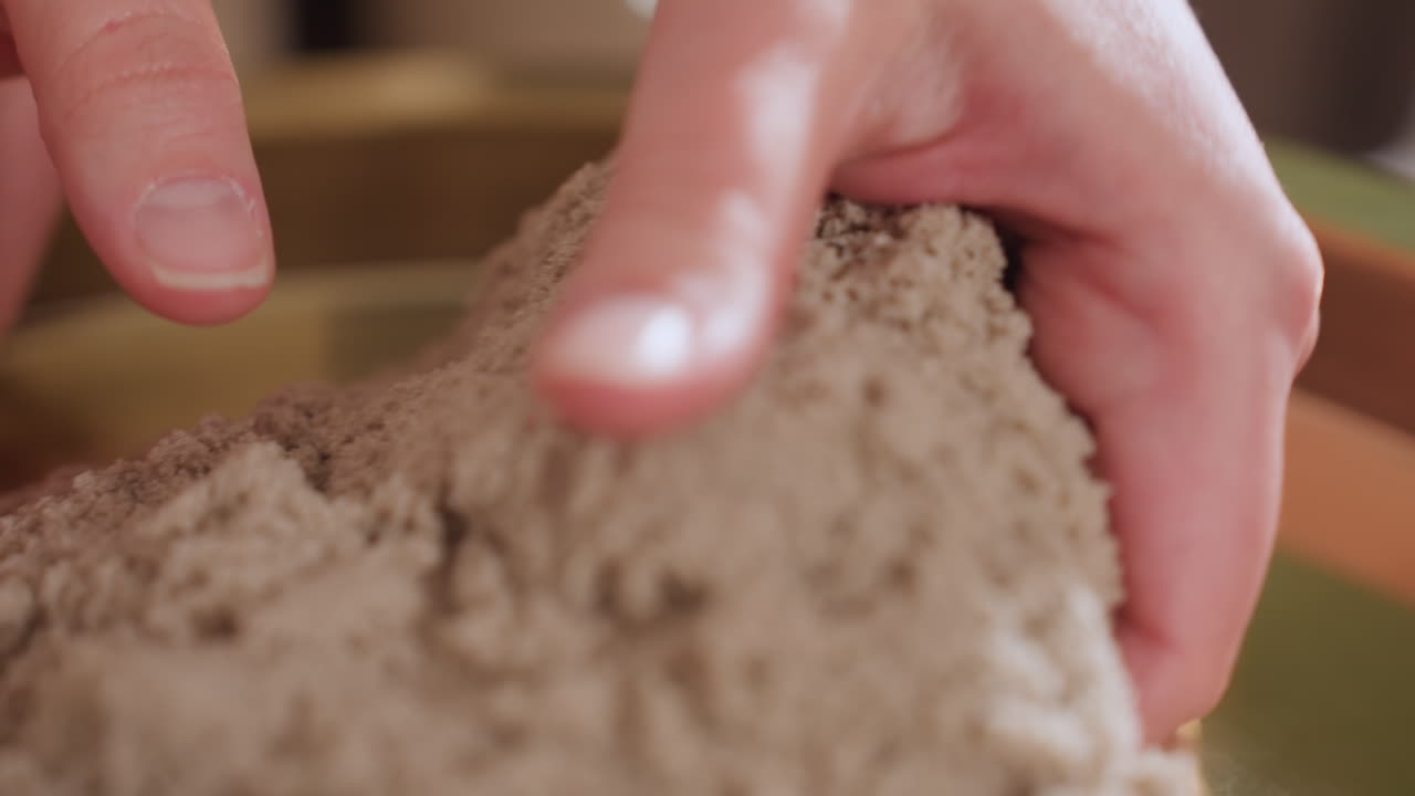 Close up of hands lifting soft clay mold from gold tray during therapeutic art session guiding tactile engagement in serene room for mindfulness creative expression during counseling
