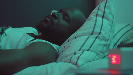 hombre afroamericano sin sueño acostado en la cama y mirando el reloj en la noche