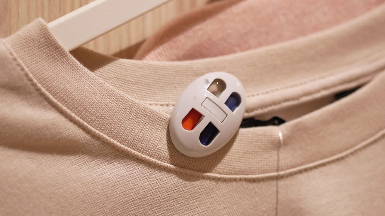 Close up of a security tag attached to a beige shirt hanging on a hanger