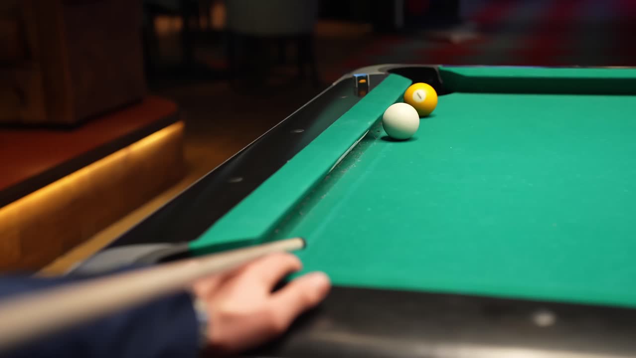 Close-up of a billiards cue shot on a green pool table as the yellow ball drops into the corner pocket, with cue ball near the rail, filmed indoors with shallow depth of field