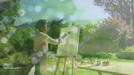 animation of light spots over african american woman painting on easel in garden