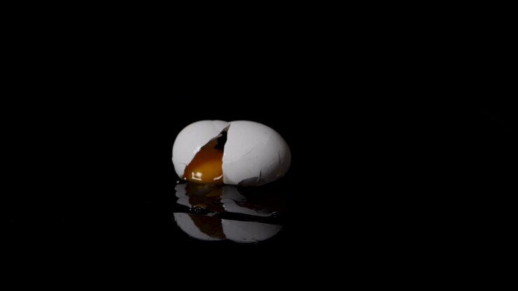 Egg cracks and gets splattered on a black surface