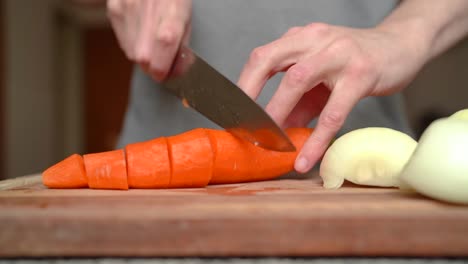 clean carrot being sliced on wooden cutting board, white onions next