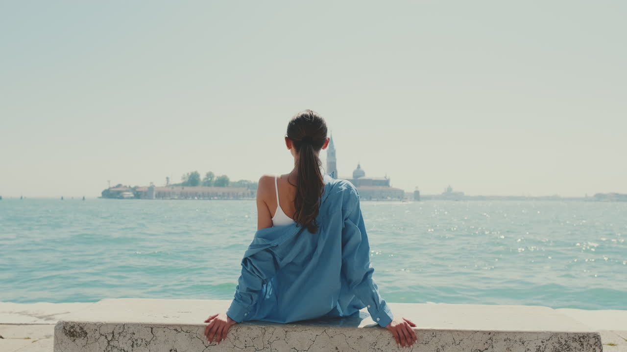 Young Woman Sitting by the Water Looking at a Distant City
