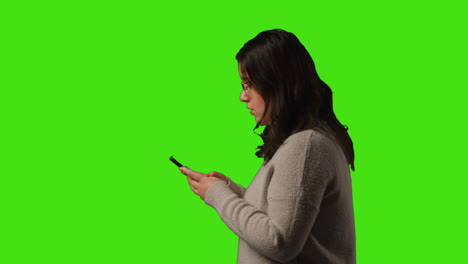 young woman walking into frame making call on mobile phone standing against green screen studio background