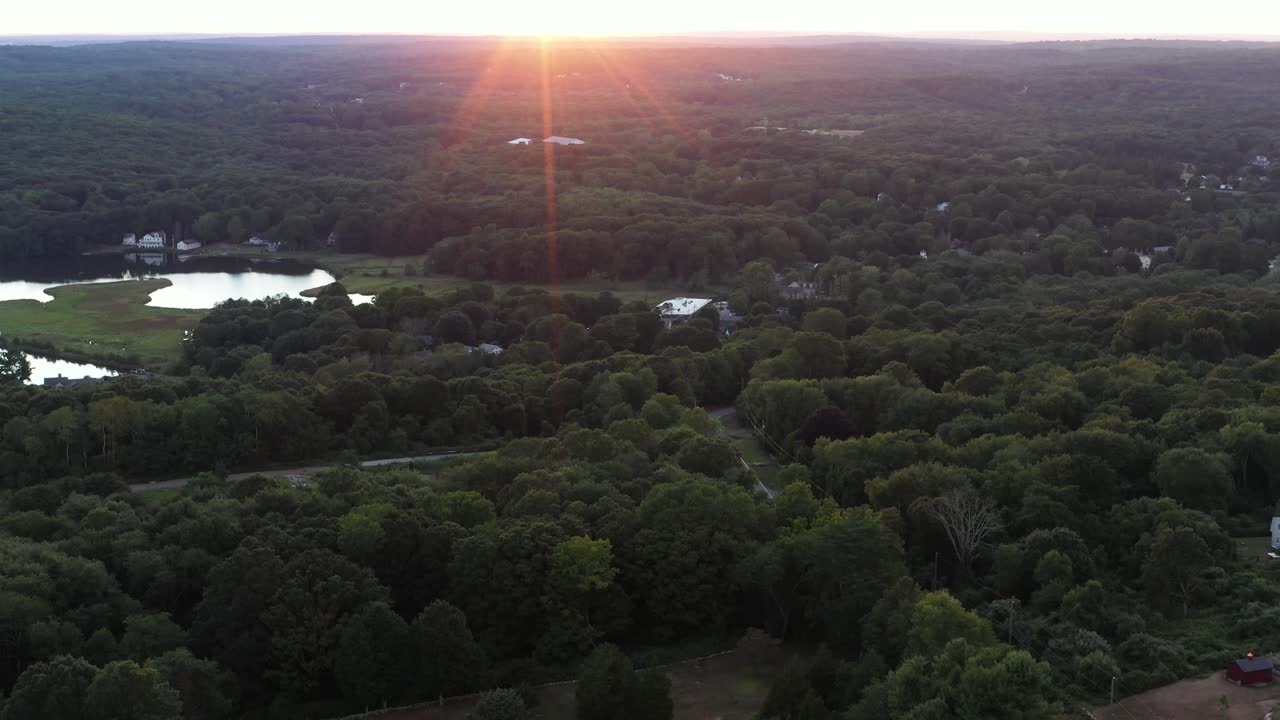 reverse aerial shot over rural area of the Northeastern USA at summer sunset, with lens flare