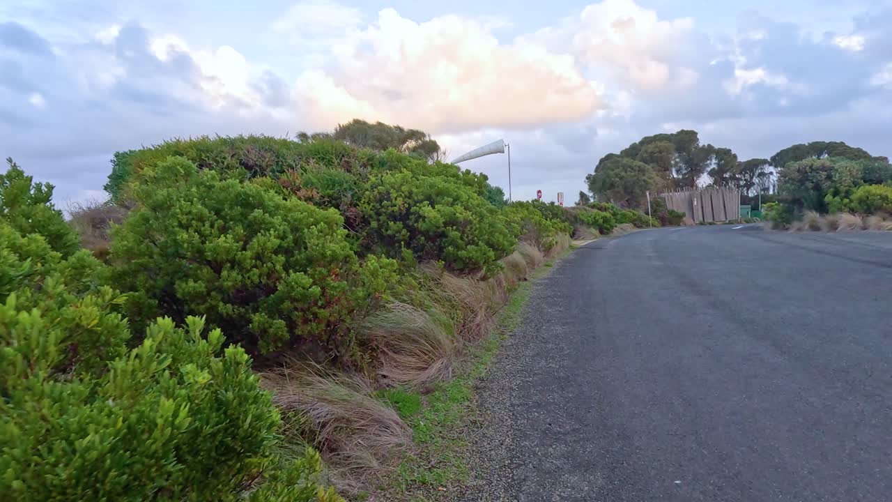 잔잔한 초록색으로 둘러싸인 휘어지는 길을 따라 조용한 운전, 부분적으로 구름이 가득한 하늘 아래, 자연의 본질을 포착