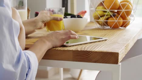 parte de una mujer usando una tableta y bebiendo jugo de naranja en la cocina
