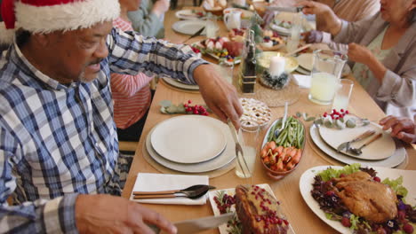 happy diverse senior male and female friends serving food at christmas dinner table, slow motion