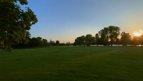 Zeitraffer-Der-Untergehenden-Sonne-Im-Kölner-Rehnpark-Hinter-Den-Bäumen-Mit-Dem-Kölner-Dom-Am-Horizont-Und-Einigen-Menschen,-Die-Abends-Spazieren-Gehen