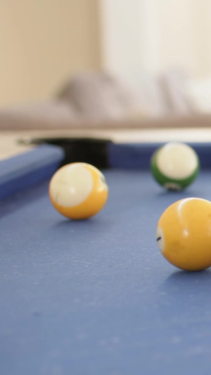 Vertical video: Rolling yellow solids, striped and green balls moving on blue-felt pool after hit