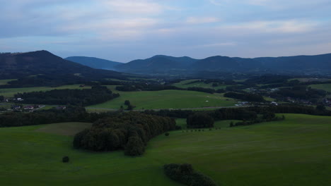 Vista-Aérea-De-Un-Paisaje-Lleno-De-Colinas-Durante-La-Tarde-Y-Montañas-En-El-Fondo