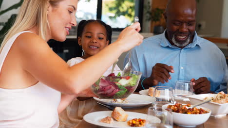 multi-generation family sitting around table serving food for meal at home