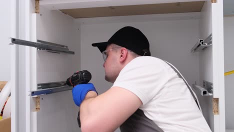 a young man collects kitchen furniture installation of furniture hinges on cabinet doors a young man collects kitchen furniture installation of furniture hinges on cabinet doors focused professional worker in uniform assembles furniture in kitchen