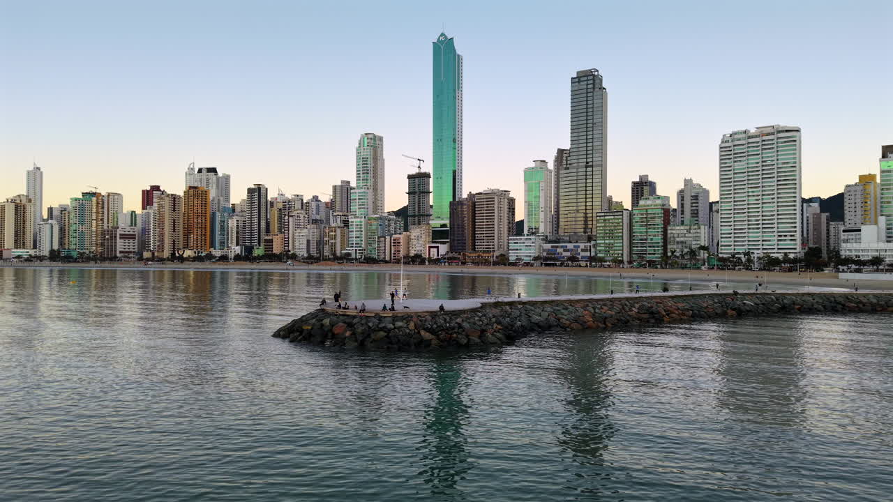 Soft sunrise light over Balneario Camboriu skyline, calm bay and stone jetty seen from above