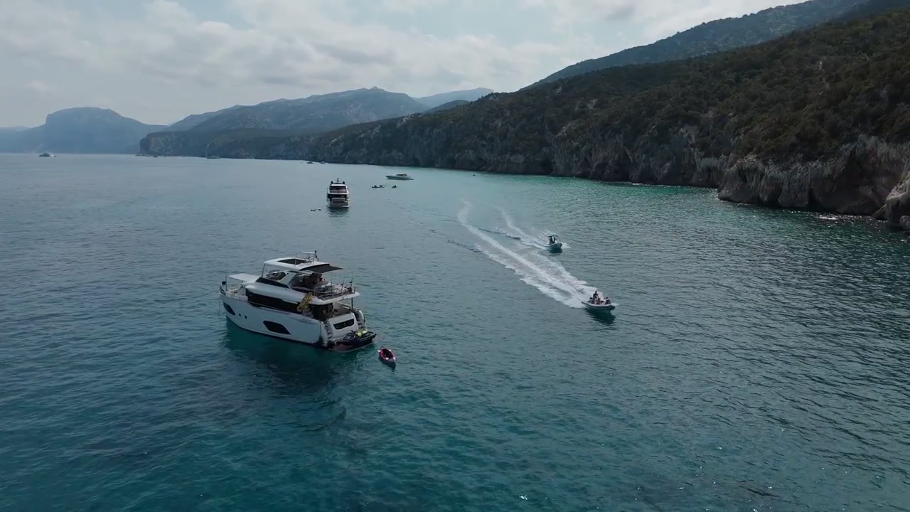 Veduta aerea serale di yacht ancorati nelle acque limpide vicino alla Spiaggia di Cala Fuili, Sardegna, Italia, che mostra la frastagliata costa mediterranea e il tranquillo paesaggio costiero.