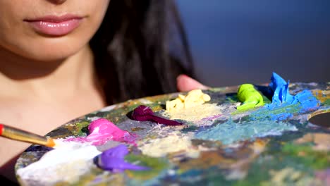 summer,outdoors, close-up of a palette with paints, the woman artist mixes paints with a brush on the palette