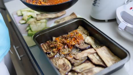 pouring cooked ground meat with sauce on top of eggplant slices in tray for baking