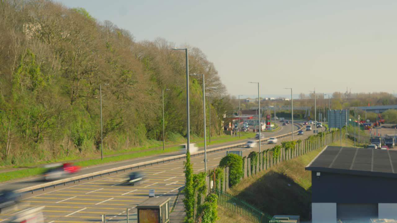 Fast Timelapse of Cars and Trucks with Motion Blur Passing Busy Road Near Trees with Blue Sky Background.