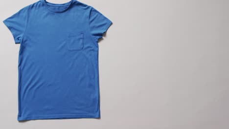 video of flat lay of blue t shirt with copy space on white background