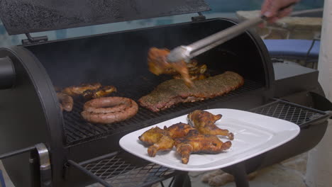 el hombre saca los muslos de pollo de barbacoa de la parrilla de fumar y en el plato