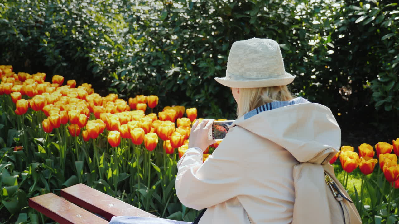 menina em um banco fotografa tulipas laranja