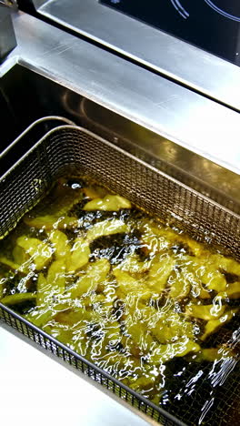 cooking fries in deep fryer. frying potatoes in restaurant fryer basket. vertical video