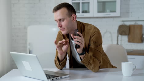 shopping online. young man freelancer talking in front of a laptop and proposes new device. smiling guy working through the laptop computer at home. remote job.