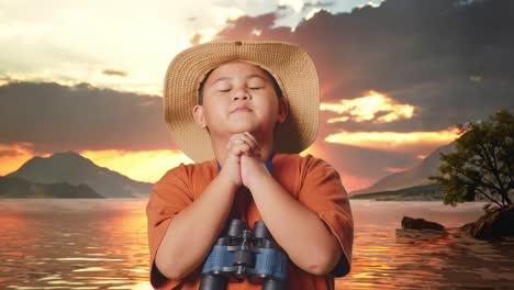 asian boy with a hat and binoculars praying for something at a lake. boy researcher examines something, travel tourism adventure concept, close up