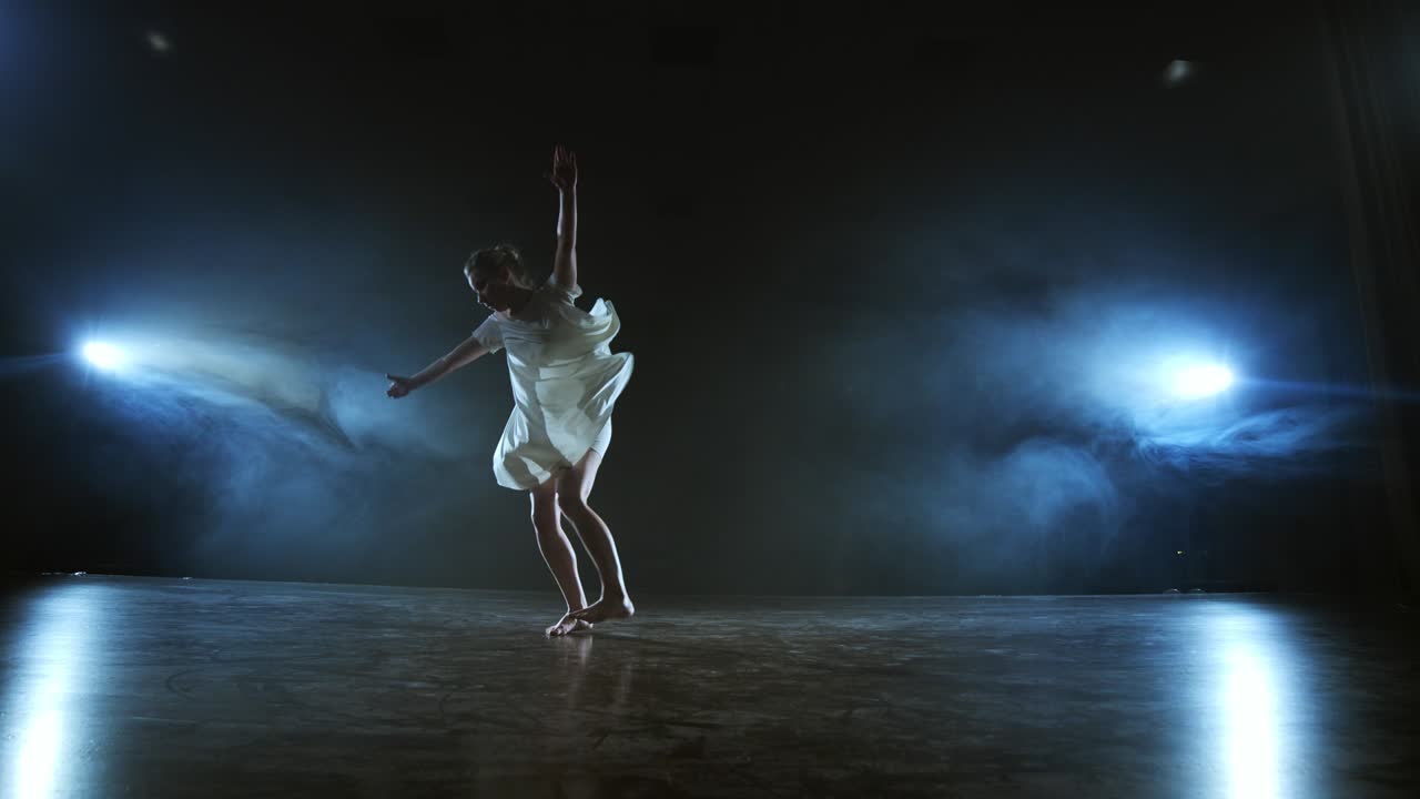 Modern ballet dancing woman barefoot doing spins and pirouettes and dance steps standing on stage in smoke in slow motion. Performance on stage