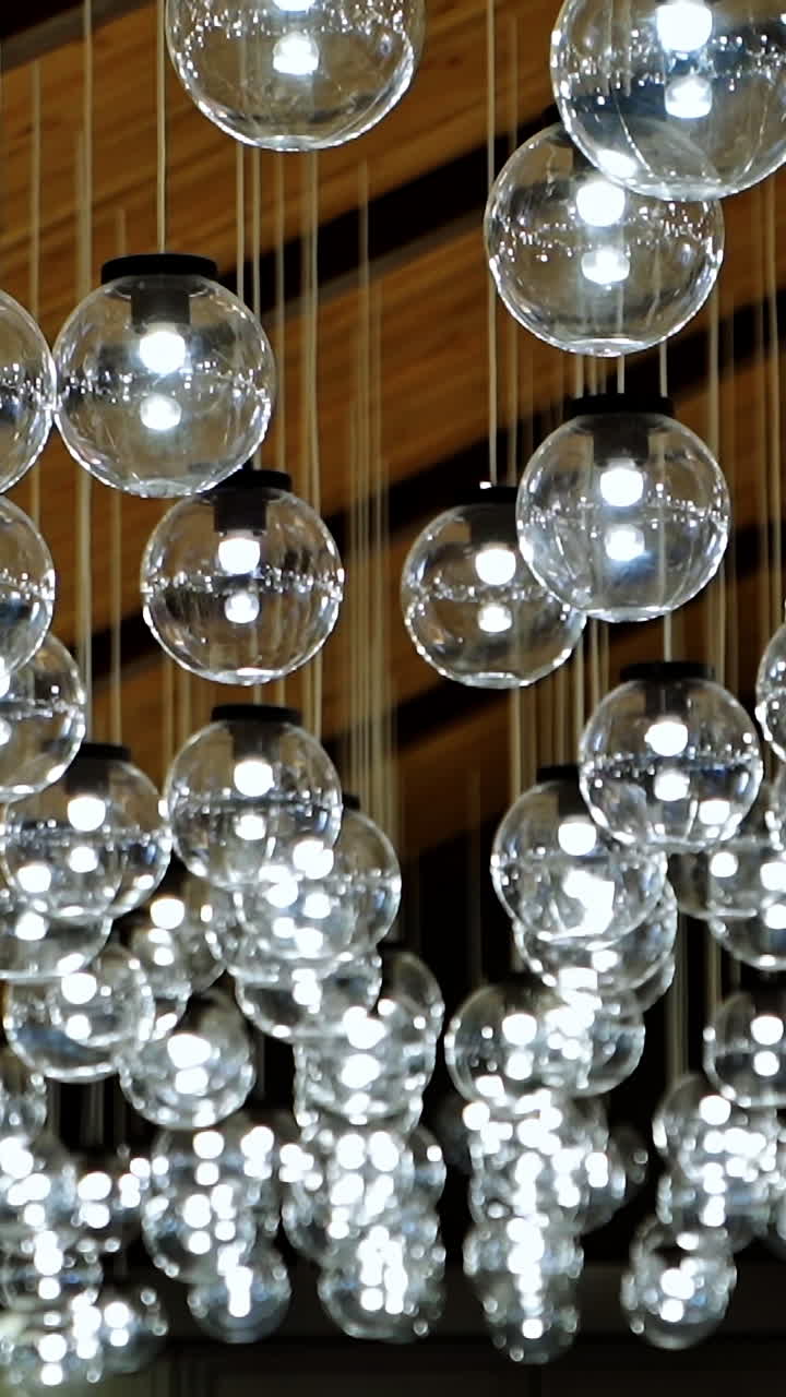 Luxury interior of sparkling lamps. Blurred view of modern ceiling lighting of hanging light bulbs balls indoors. Vertical video