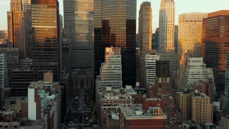 Forwards-fly-above-buildings-in-midtown.-Modern-skyscrapers-with-glossy-facades-reflecting-colourful-sunset-sky.-Manhattan,-New-York-City,-USA