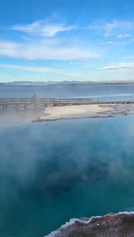 Yellowstone-Nationalpark,-Wyoming,-USA,-Vertikale-Ansicht-Des-Blauen-Geothermischen-Wassers-Und-Der-Frau-Auf-Einem-Holzpfad-Am-See