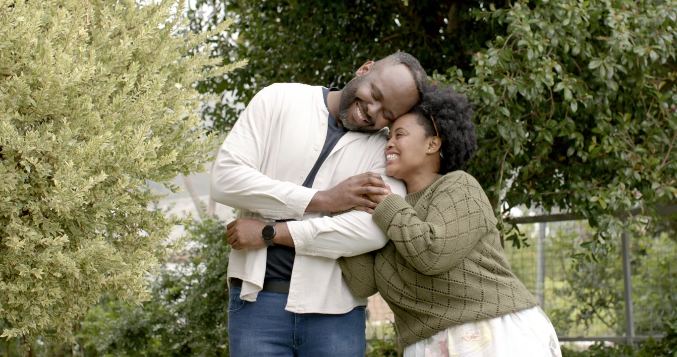 African American couple in garden, woman reaching, holding man's forearm and watch, showing love