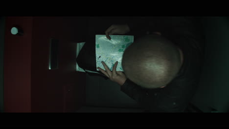 a bald dangerous looking man unpacks a black bag in the public toilet