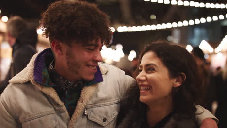 Retrato-De-Una-Pareja-Joven-Disfrutando-Del-Mercado-Navideño-Por-La-Noche