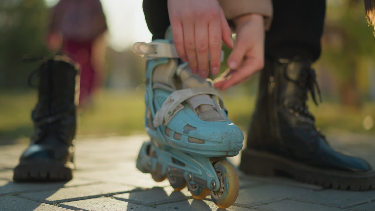 한 발이 검은색 부츠에 남아있는 동안 밝은 파란색 롤러블레이드의 을 조정하는 사람의 클로즈업. 초점은 손과 롤러 블레이드, 다른 부츠가 보입니다.